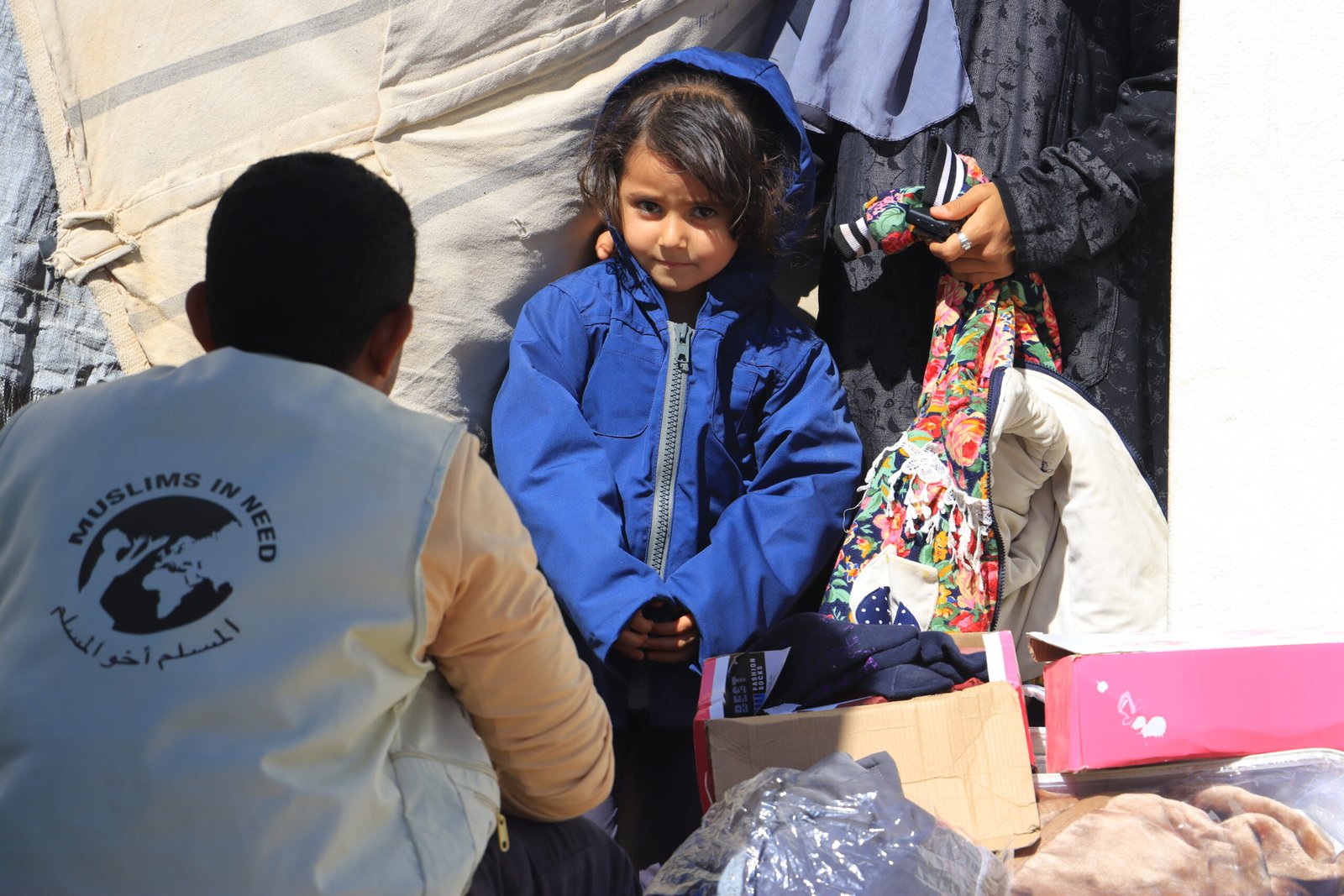 A Muslims In Need team member supporting a child wearing a winter coat